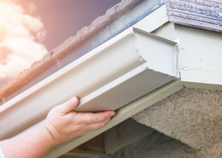 Hands installing new seamless gutters on a home, demonstrating professional gutter installation for improved water drainage.