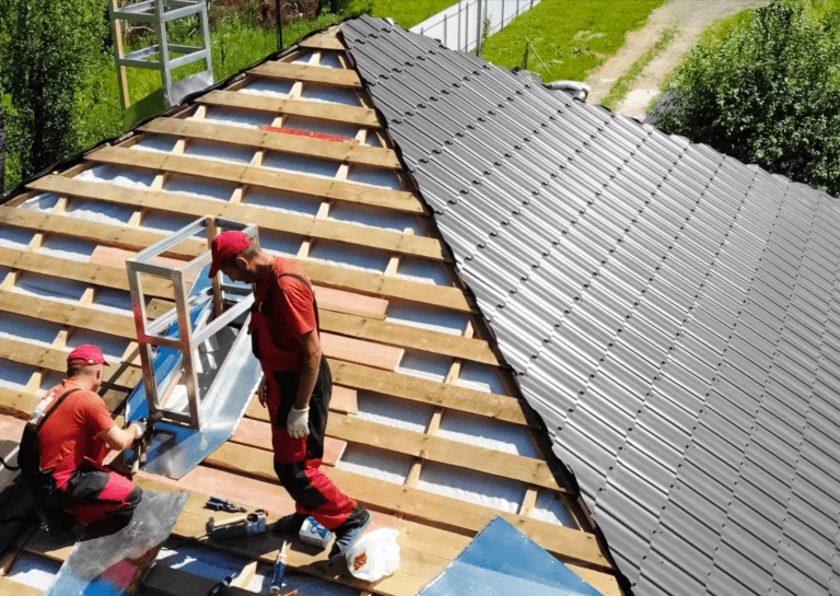 Two workers installing a residential roof with metal panels, showcasing a professional roof installation process.